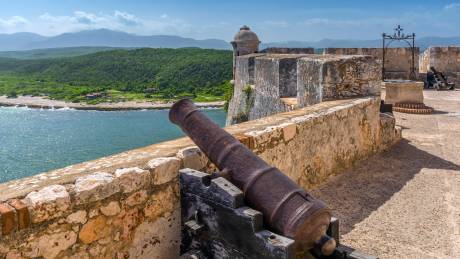 An ancient cannon guards the historic fortress overlooking a lush green coastline and the sparkling blue sea.
