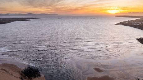 Golden sunset hues paint the sky over a serene ocean, casting gentle waves upon a sandy shore.