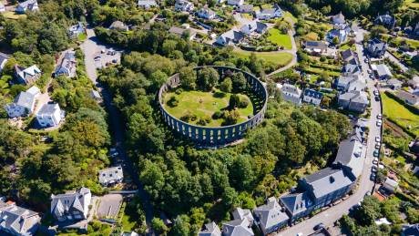 An aerial view captures the unique circular ruins of a historic structure nestled amidst lush green trees and a charming village.