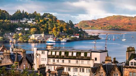 A charming coastal town is bathed in the warm glow of autumn sunlight, with boats dotting the harbor and hillsides ablaze with color.