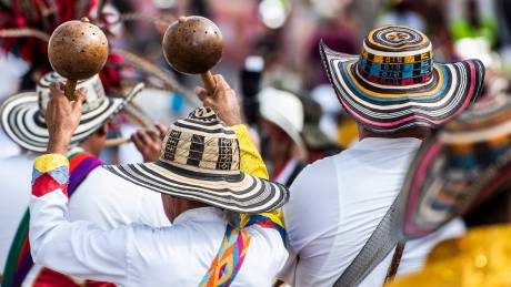 Musicians in traditional Colombian hats and colorful attire play maracas during a vibrant festival celebration.
