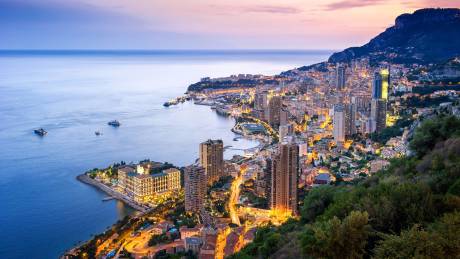 Monaco's glittering coastline and illuminated cityscape shimmer under the twilight sky.