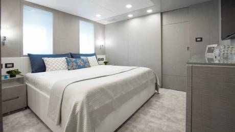 A modern and minimalist bedroom with a large bed, white bedding, and blue and white patterned pillows, set against a backdrop of gray walls and built-in storage units.
