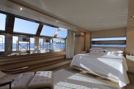 Luxurious yacht cabin offers panoramic ocean views from a comfortable bed and seating area.