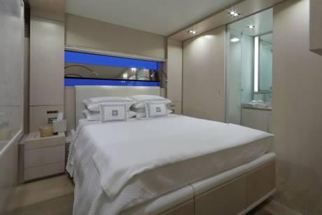 Luxurious white bedding adorns a master stateroom with a vibrant blue window view and an adjoining glass-enclosed shower.