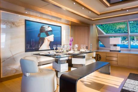 A modern dining area aboard a yacht features a striking art piece and a glass-topped table set for a meal.