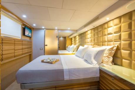 Luxurious yacht cabin features a plush bed with a breakfast tray and a golden tufted headboard.