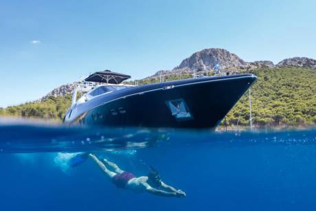 A snorkeler enjoys the clear blue waters near a luxurious yacht anchored off a lush, mountainous island.