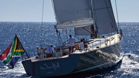 A sleek sailboat with the South African flag proudly displayed cuts through the sparkling blue ocean waters.