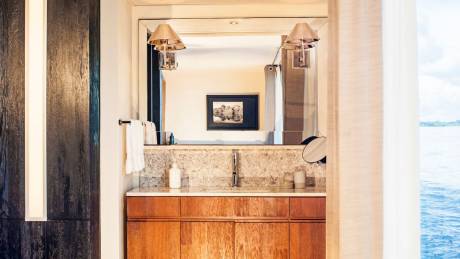 A luxurious bathroom vanity with wooden cabinets and a marble countertop overlooks a tranquil body of water.