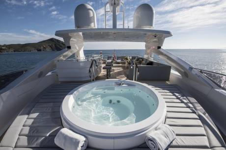 Relax in the jacuzzi on the deck of this luxurious yacht, overlooking a stunning coastal landscape.