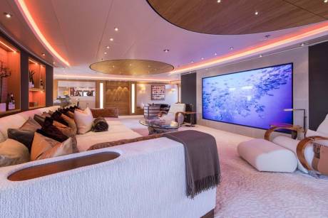 This luxurious yacht lounge features a massive screen displaying a school of fish, complemented by ambient lighting and plush seating.