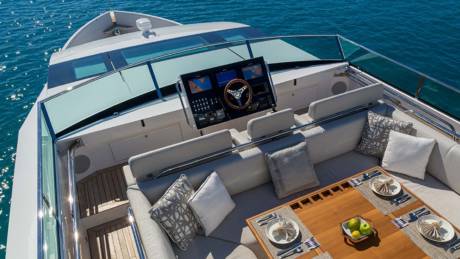 A luxurious yacht deck is set for dining with elegant place settings and comfortable seating overlooking the sparkling blue ocean.