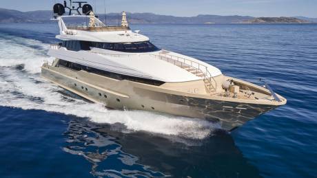 A sleek, modern yacht cuts through the deep blue sea, leaving a foamy wake under a clear sky.