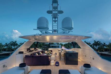 Luxurious yacht deck offers plush seating and a sleek bar area against a backdrop of palm trees at twilight.