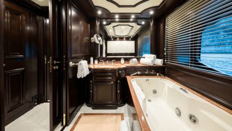 Luxurious dark wood cabinetry and a spacious bathtub create an opulent retreat with a view of the sparkling blue water.