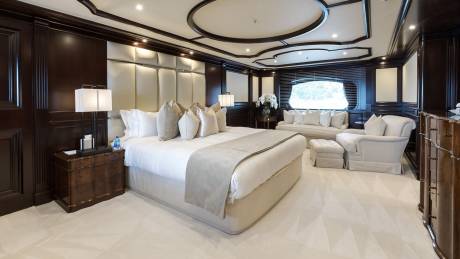 Luxurious yacht master suite features a king-sized bed, plush seating, and elegant dark wood paneling.