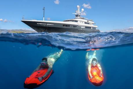 Two people enjoy a sunny day riding underwater scooters near a luxurious yacht.
