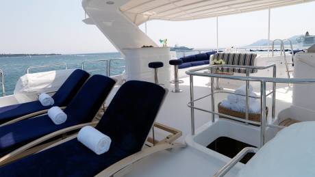 Relax on plush navy loungers with rolled towels, enjoying drinks at the bar with a cruise ship in the distance.