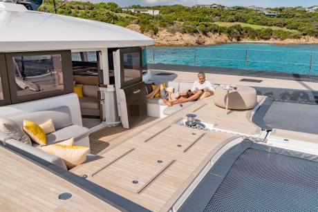 A couple relaxes on the deck of a luxurious catamaran, enjoying the turquoise waters and lush green coastline.