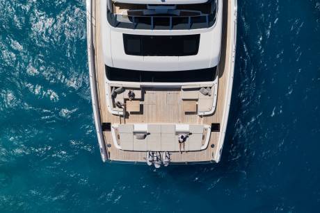 Two people relax on the spacious deck of a luxurious yacht cruising through clear blue waters.