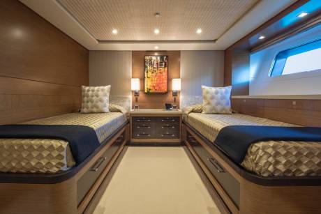 Luxurious twin beds with textured gold bedding and dark blue throws offer a serene retreat in this elegant stateroom.