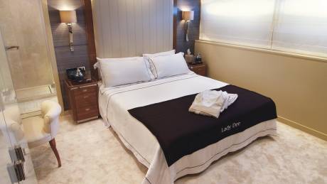 A luxurious yacht cabin features a neatly made bed with a dark throw blanket embroidered with "Lady Dee."