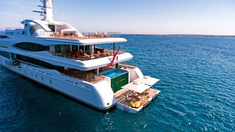 The luxurious superyacht Lady Christine cruises through calm blue waters under a clear sky.