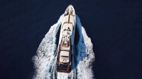 A luxurious white yacht cuts through the deep blue ocean, leaving a dramatic trail of white wake.