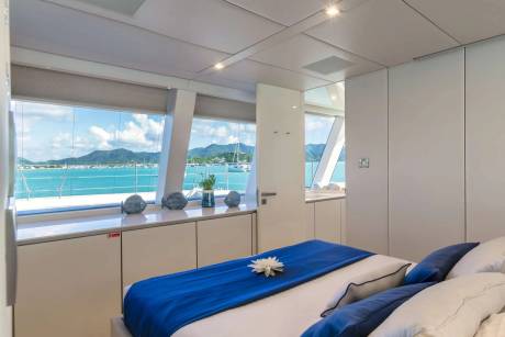 A luxurious yacht cabin offers stunning ocean views and a comfortable bed adorned with a vibrant blue runner.
