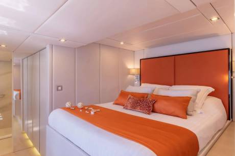 A luxurious bedroom features a vibrant orange headboard and runner on a crisp white bed.