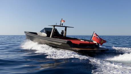 A sleek, dark boat cuts through the blue ocean, leaving a white wake under a clear sky.