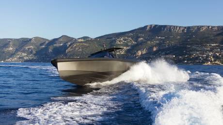 A sleek motorboat cuts through the azure waters, leaving a dramatic white wake against a backdrop of verdant, cliffside towns.