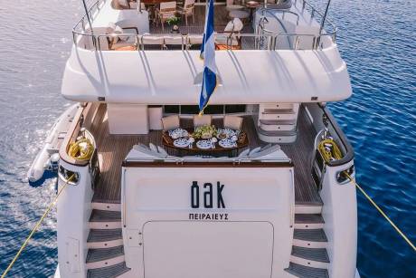 A luxurious yacht named "Oak" is moored in the clear blue waters of Greece, ready for an elegant seaside dining experience.