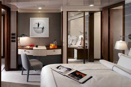A luxurious yacht cabin features a sleek desk, a comfortable bed, and elegant wooden accents.