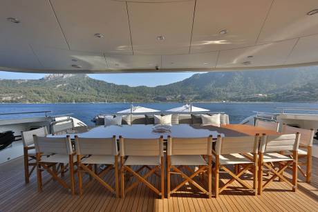 Enjoy al fresco dining with a stunning view of lush green mountains meeting the azure sea from this yacht's spacious deck.