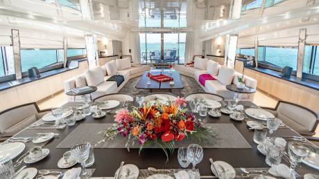 A beautifully set dining table on a yacht awaits guests with a vibrant floral centerpiece and stunning ocean views.
