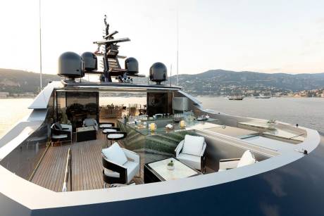 Luxurious yacht seating and bar area offer stunning views of a coastal town at sunset.