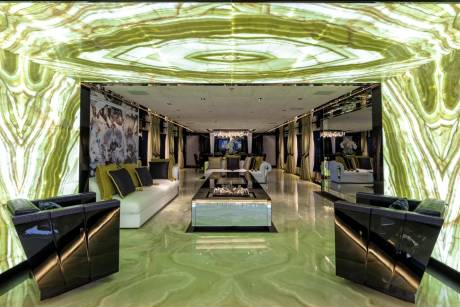 This opulent living space features luminous green onyx walls and floors, complemented by plush white sofas and a sleek glass coffee table.