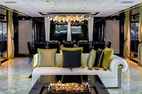 Luxurious yacht interiors feature a white leather sofa with decorative pillows facing a modern fireplace and a formal dining area.