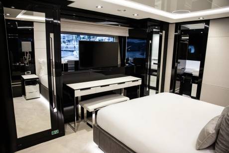 A luxurious yacht cabin features a sleek black and white design with a large television, vanity, and comfortable bed overlooking the water.