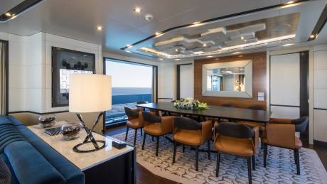 A modern dining area with a large table and comfortable chairs offers stunning ocean views through a panoramic window.