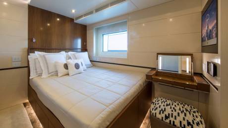 A luxurious yacht cabin features a comfortable bed, a vanity with a lighted mirror, and a wall-mounted television displaying a mountain scene.