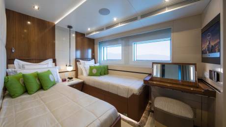 Luxurious twin beds with plush green pillows are bathed in warm light within this elegant yacht cabin.