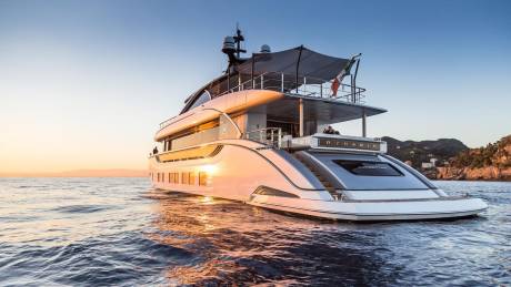 A luxurious yacht glides across the calm sea at sunset, reflecting the golden light and the distant Italian coastline.