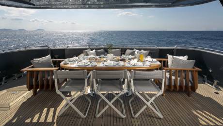A beautifully set table awaits a delightful breakfast on the deck of a luxury yacht, overlooking the sparkling sea.