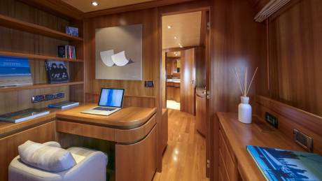 A cozy wooden desk area with a laptop and bookshelves offers a quiet workspace aboard this luxurious yacht.