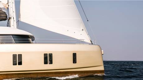 A sleek, modern catamaran glides through the deep blue water under a vast, pale sky.