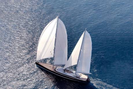 A majestic yacht with billowing white sails glides gracefully across the sparkling blue ocean.