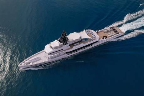 A sleek white superyacht glides through the deep blue ocean, leaving a foamy wake behind.